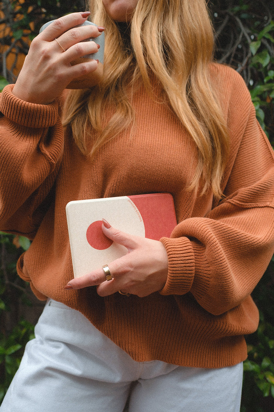 Person wearing an orange sweater holding a Ch 4 Kindle Cover - Balanced Yin Yang with greenery in the background